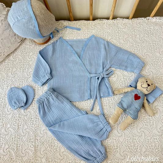 Bebe mavi renkli, 4 parçadan oluşan erkek bebek alt üst takımı, kruvaze yaka body ve şapka içerir.